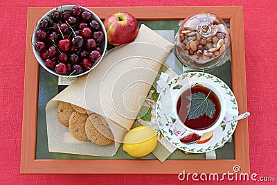 Still life with tea, homemade oatmeal cookies with raisins, cherries, lemon, apple, nuts and lump sugar on a wooden tray Stock Photo