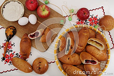 Still-life with traditional Russian pies, ingredients - flour, eggs, apples. On authentic tablecloth with a wooden spoon with a pa Stock Photo