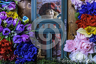 Young girl doll looking out screen door at spring flowers Editorial Stock Photo