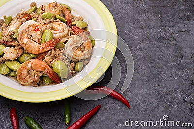 Bitter peas stir-fried with fresh prawns or Sato stir-fried prawns in a green dish and with fresh chilies laid on the black table Stock Photo