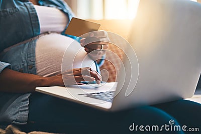Stocking up before baby arrives. a pregnant woman using a laptop and credit card on the sofa at home. Stock Photo