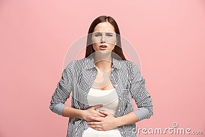 The stomach ache. The sad woman with stomach ache or pain on a pink studio background. Stock Photo