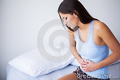 Stomach Pain. Unhealthy young woman with stomachache leaning on the bed at home Stock Photo