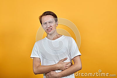 Stomach pains stomach problems white T-shirt young male on yellow background. Stock Photo