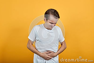 Stomach pains stomach problems white T-shirt young male on yellow background. Stock Photo