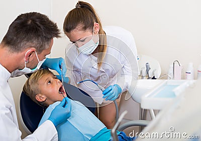 Stomatologist man with girl assistant are diagnosticating to young patient which is sitting Stock Photo