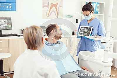 Stomatologist nurse in gloves holding tablet showing jaw x-ray to sick patient Stock Photo