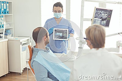 Stomatologist nurse pointing on digital screen explaining tooth x-ray to sick man Stock Photo