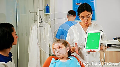 Stomatologist woman looking at green screen tablet while speaking with mother Stock Photo