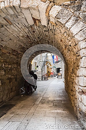 Stone arch connecting the old medieval streets of Trogir in Croatia with a motorcycle and the flag of Croatia Editorial Stock Photo