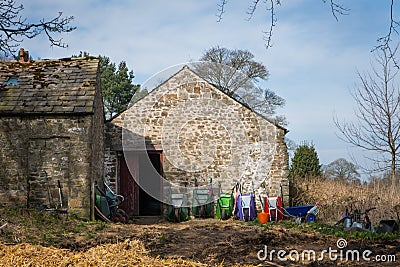 A stone barn on a rural farm with colourful wheelbarrows against the wall Stock Photo