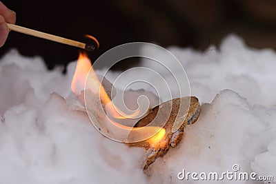 Stone of Calcium carbide calcium acetylide burn with big flame in white snow. Piece of carbide react with water from snow and Stock Photo