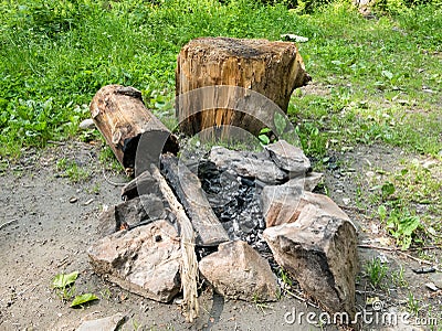 Stone camp fire pit with a log or stub for sitting down . Burnt wood in a camp fire Stock Photo