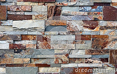 Stone cladding wall made of natural stones of different shapes. The main colors are red, gray,orange and brown. Stock Photo