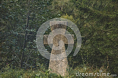 Stone concrete cross religion sigh on ground hill with forest spruce needle trees dark green moody foliage unfocused background Stock Photo