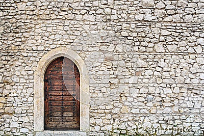 Stone fortress castle wall of a medieval castle, an old wooden closed arcade door with iron rivets. Stock Photo