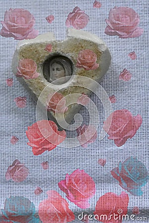 Stone of heart with the image of the Virgin Mary on a white canvas with decorative roses. Stock Photo