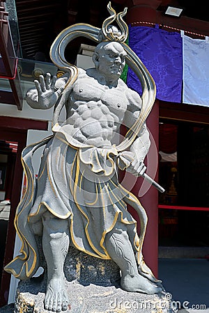 Stone image of a fierce and wrathful guardian of the Buddha, Narayana, at left entrance of a Buddhist temple in East Asia Editorial Stock Photo