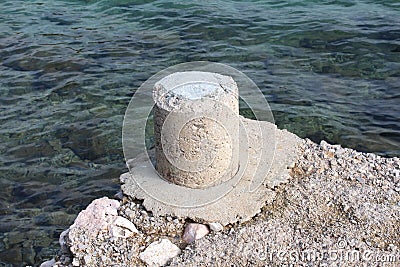 Stone mooring bollard on edge of concrete pier next to sea Stock Photo