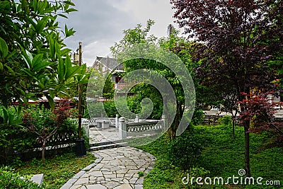 Stone path in garden before tile-roofed buildings on cloudy spring day Stock Photo