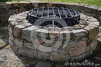 Stone round fountain with a protective grid of twisted prisms. forged steel bars go spiraled at the top. around the well there is Stock Photo