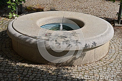 Stone sandstone circular fountain in the park. built of sandstone filled with water. lined with a light threshing gravel road with Stock Photo