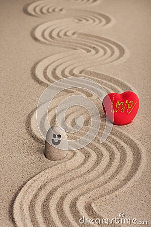 Stone smiley and a red heart stand on a zigzag from the sand. Stock Photo