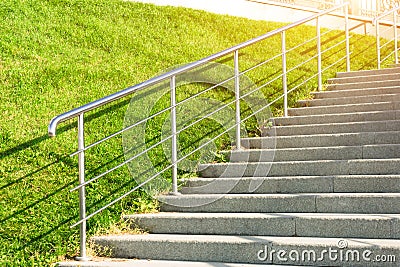 Stone staircase leading up the slope with lawn grass, with metal shining and railing. Stock Photo