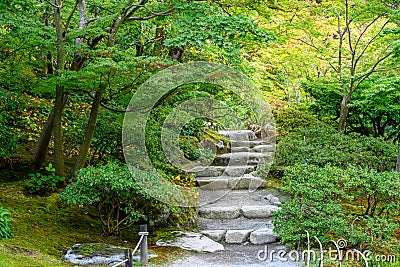 Stone steps leading into a peaceful Japanese garden full of maple trees starting to turn fall colors Stock Photo