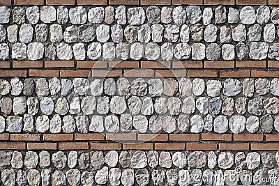 Stone wall made up of rows of white natural stones interspersed with rows of bricks. Stock Photo