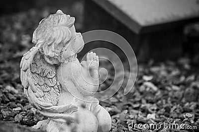 Stoned angel praying on tomb in cemetery Stock Photo