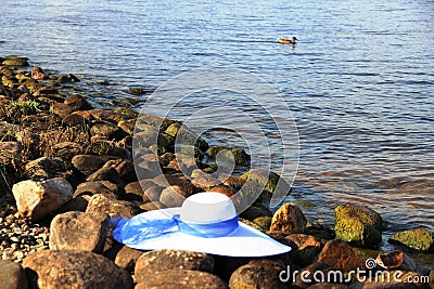 on stones Bank rivers white female hat with broad brim, blue ribbon Stock Photo