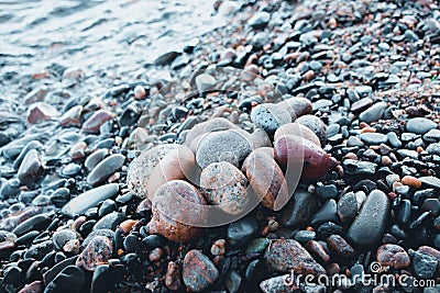 Stones of different shades and different oval shapes lie on the stony shore of a large and cold lake. Stock Photo