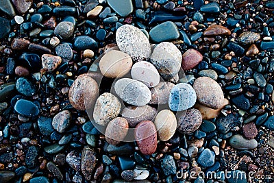 Stones of different shades and different oval shapes lie on the stony shore of a large and cold lake. Stock Photo