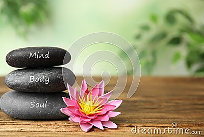 Stones with words Mind, Body, Soul and flower on wooden table, space for text. Zen lifestyle Stock Photo