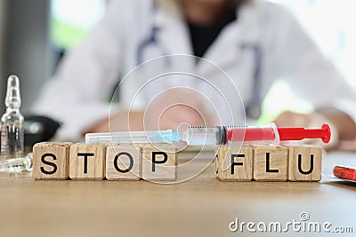 Stop flu words on wooden cubes and vaccine syringe on table, doctor in background. Stock Photo