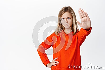 Stop. Little girl looks serious, extends one arm to say no, rejecting, prohibit action, forbid smth, standing in red Stock Photo