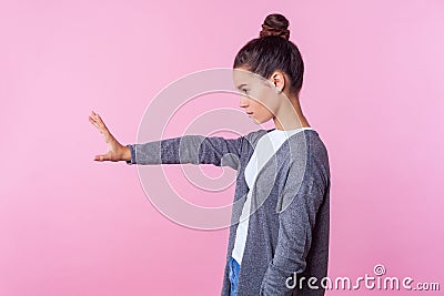 Stop! Side view of strict teenage girl standing with raised hand showing prohibition ban block gesture with palm. pink background Stock Photo