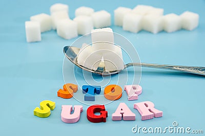 Stop sugar, text colored letters. The concept of offering diets and eating less sugar for health. White sugar cubes in a spoon on Stock Photo