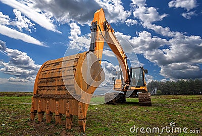 A stopped yellow excavator in a field and a beautiful sky Stock Photo