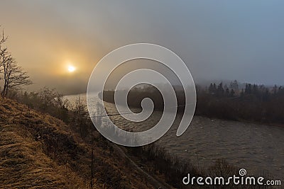 Stormy river in the mountains with a suspension bridge on a mystical misty morning. Stock Photo