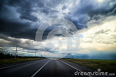 Stormy and stormy sky with gloomy dark clouds over the field and road. Dramatic landscape. The concept of traveling in Stock Photo