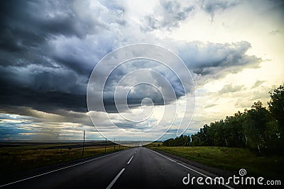Stormy and stormy sky with gloomy dark clouds over the field and road. Dramatic landscape. The concept of traveling in Stock Photo