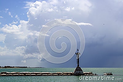 Stormy sky over ocean with a breakwater made of bags of concrete stretching out with a rustic lighthouse at the end and birds Stock Photo