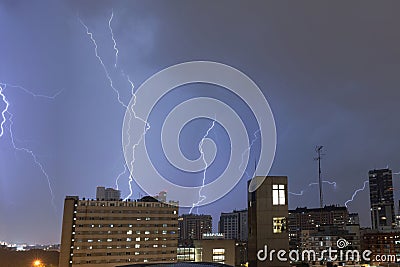 Stormy sky with several huge lightning bolts striking the ground on the outskirts of a city over buildings Stock Photo