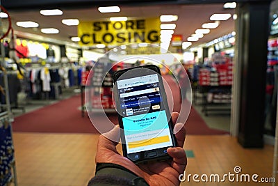 Smartphone with giant online retailer Amazon homepage in hand of customer entering a store Editorial Stock Photo