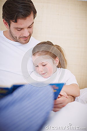 Story with a happy ending. A devoted father reading his young daughter a bedtime story. Stock Photo