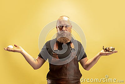 Comic portrait of muscular bearded bald man, blacksmith in leather apron or uniform isolated on yellow studio background Stock Photo