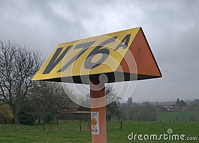 Strange yellow triangle-shaped pillar in the middle of the street with the inscription V76a in Sint-Pieters-Leeuw Editorial Stock Photo