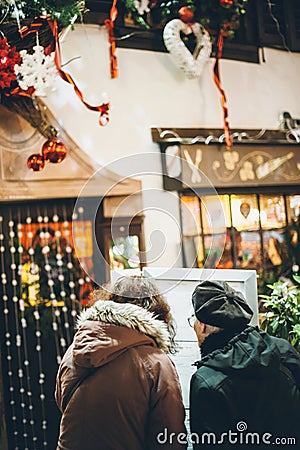 Rear view of two women looking at the restaurant menu on the street with Christmas decoration on the facade of the Editorial Stock Photo